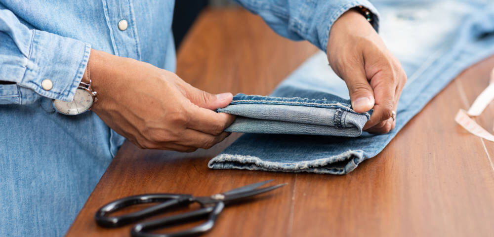 Tailor working with blue denim jeans. Tailor hem the blue jeans.